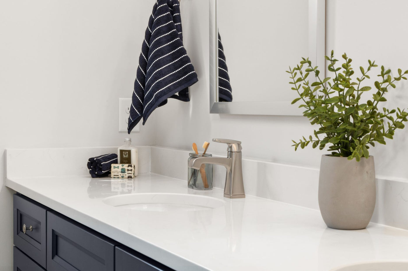 Bright modern bathroom vanity with a potted plant and striped towel.