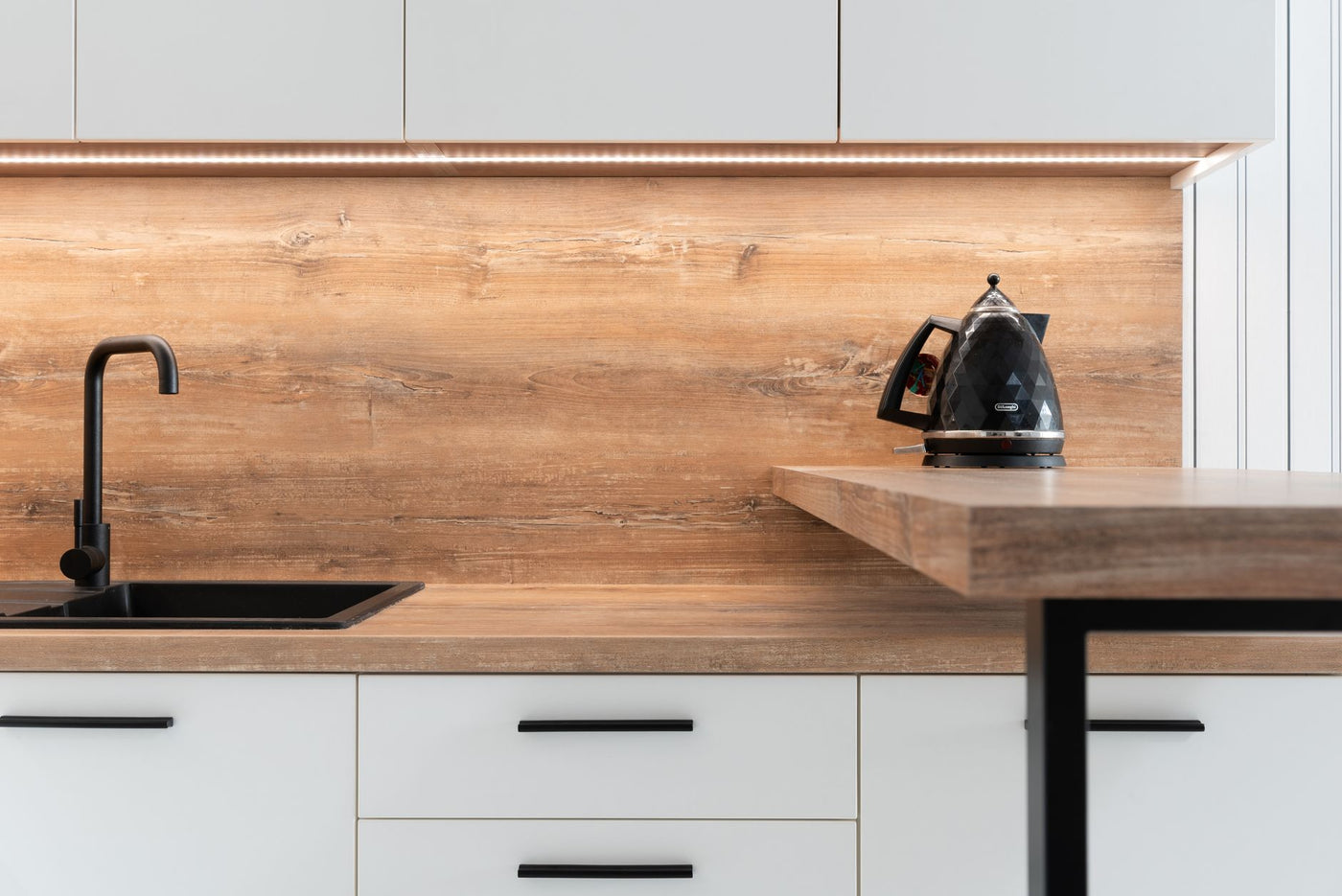 Fragment of interior of contemporary kitchen with white cabinets and wooden details in minimalist style apartment